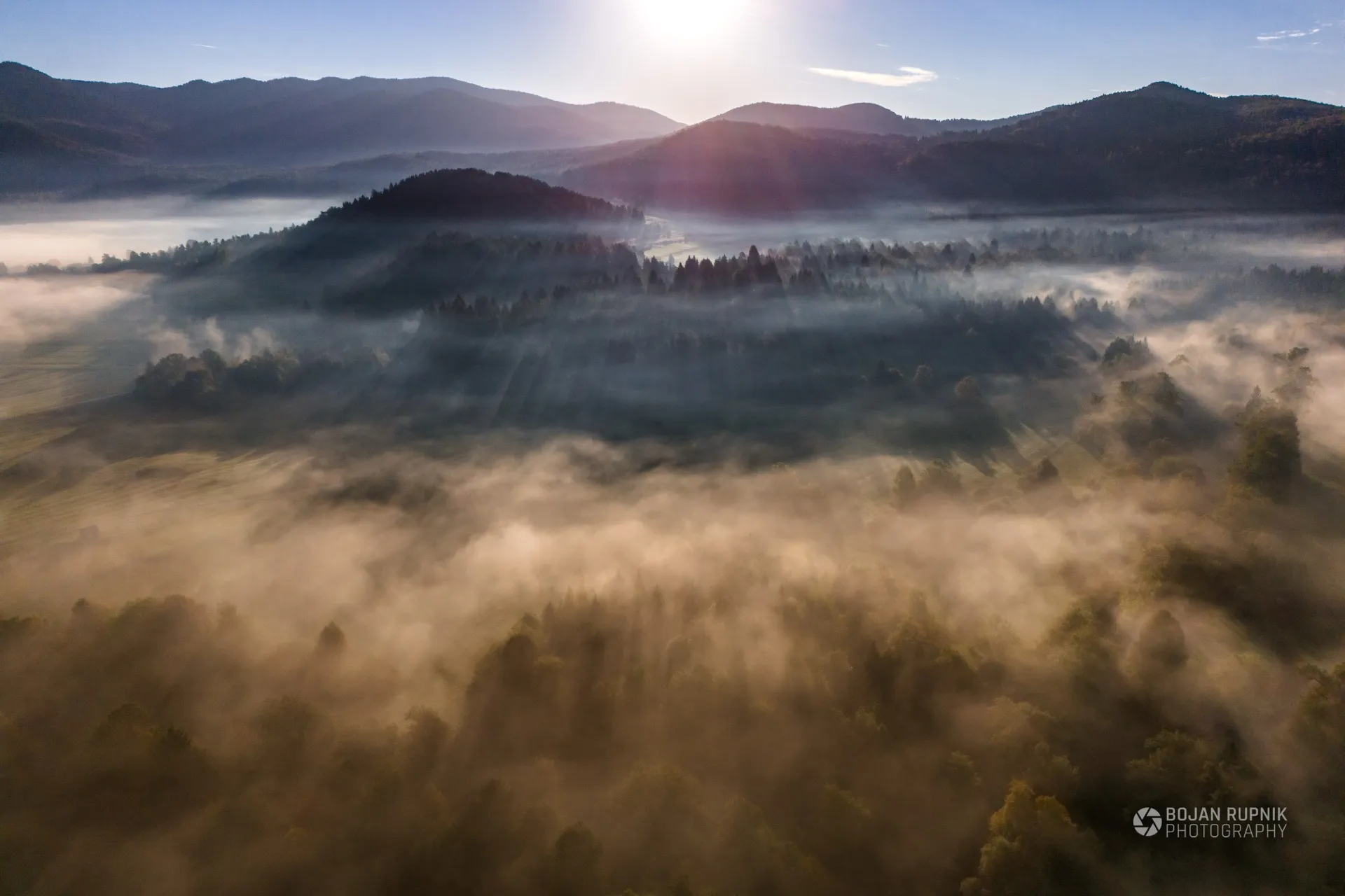 Jutranja megla nad gozdnato pokrajino in hribi v soncu, posnetek iz zraka