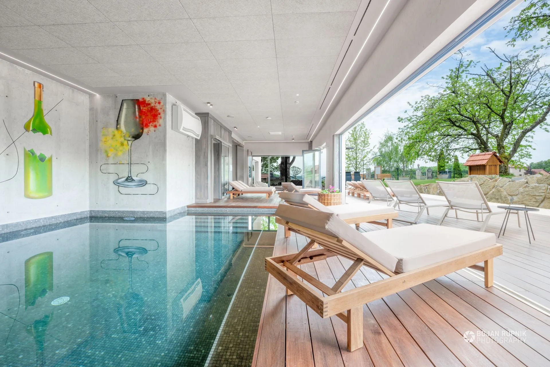 Hotelski wellness z notranjim bazenom in ležalniki ob steklenem pročelju