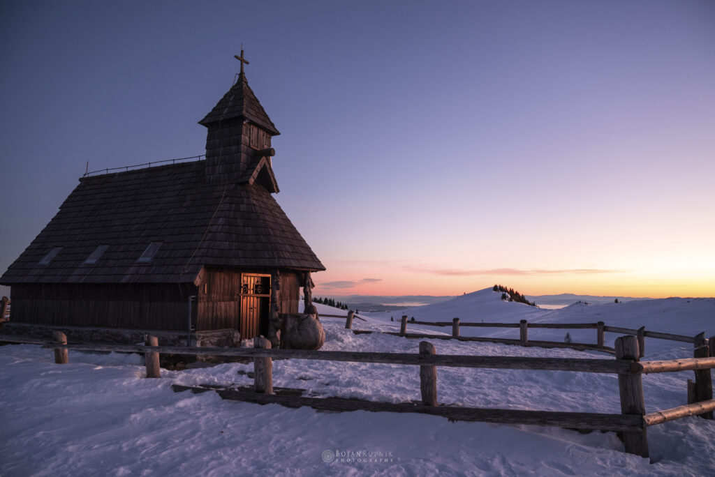 Zasnežena lesena cerkvica ob sončnem zahodu