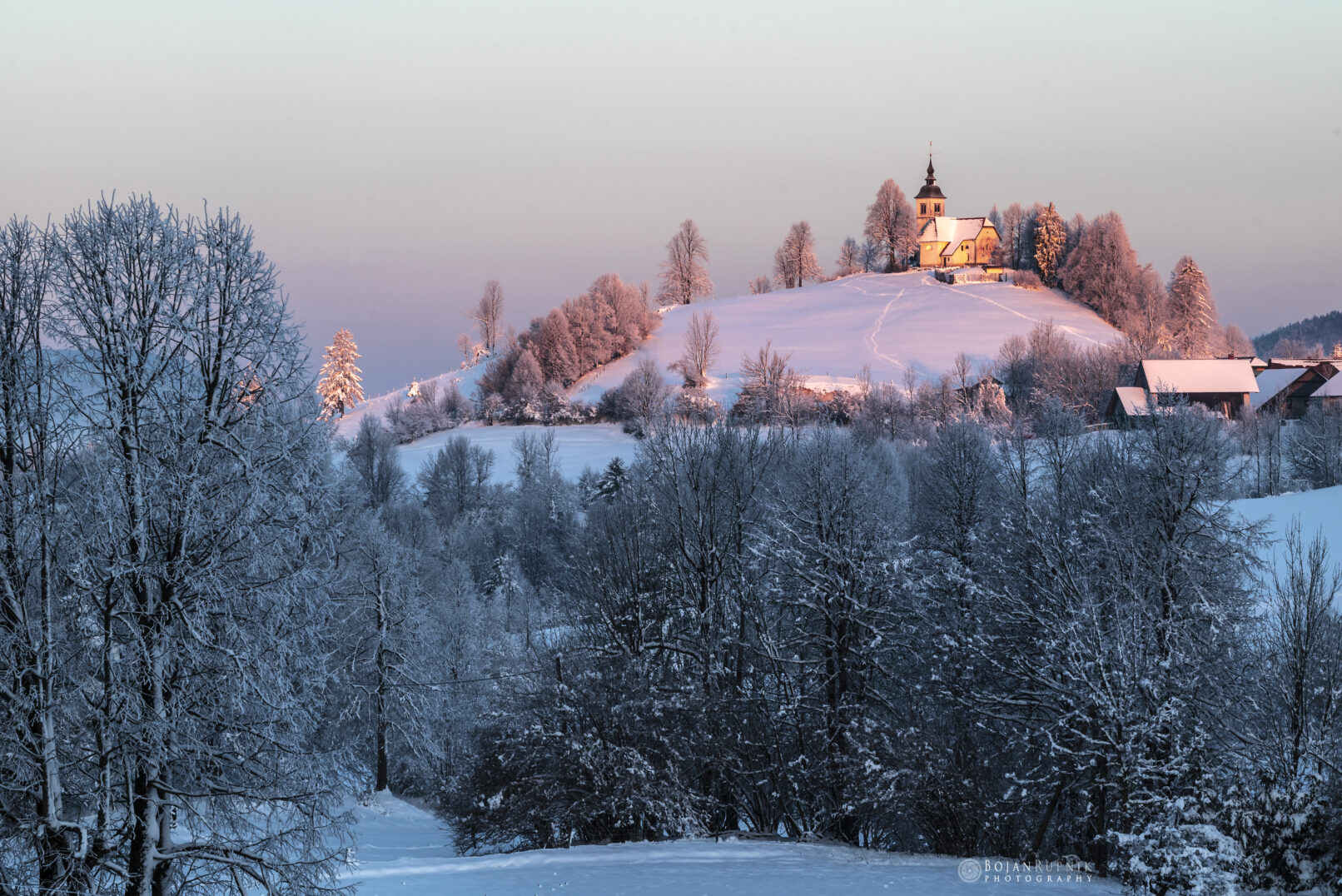 Zimsko jutro s zasneženo pokrajino in cerkvico na hribu