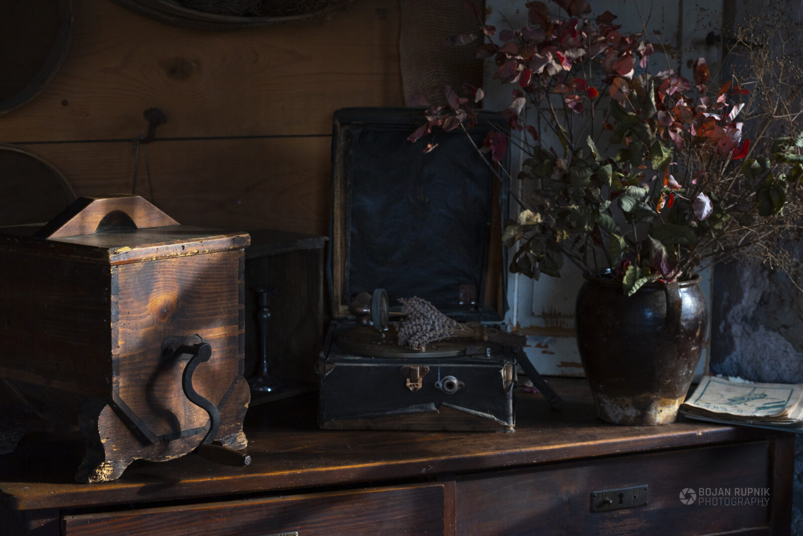 Starinski gramofon, lesen mlinček in lončena posoda s suhim cvetjem.